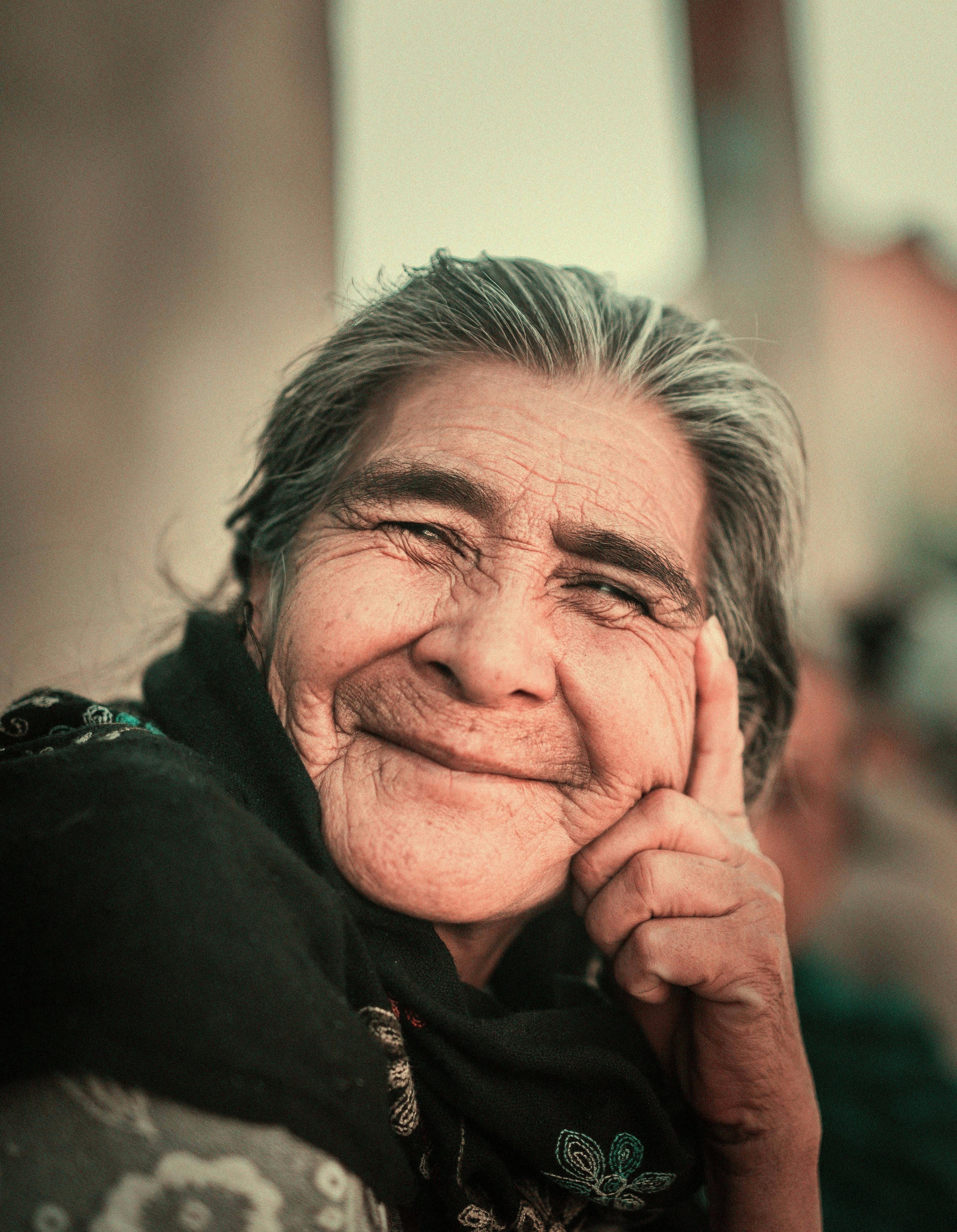 Close-up of an elderly woman with a warm smile, wearing a dark scarf.